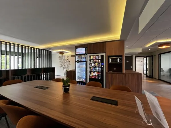 Moderne kantineruimte aan de Burgemeester Verderlaan met houten vergadertafel, snack- en drankautomaten, en een magnetron.